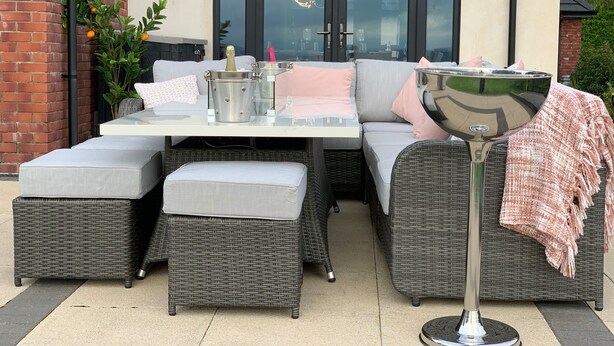 An outdoor seating area with wicker furniture, a table with a metal bucket, and a glass door in the background. - Ty Marlyn (Swansea)