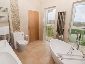 A modern bathroom with a freestanding bathtub, a toilet, and a shower area. - Ty Marlyn (Swansea)