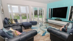 A modern living room with two black leather sofas, a glass coffee table, and a large flat-screen TV mounted on the wall. - Ty Marlyn (Swansea)