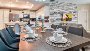 Een moderne keuken met witte kasten, een ingebouwde oven en een magnetron. Er is een eethoek met een houten tafel, gedekt voor vier personen, omringd door grijze stoelen met bekleding.