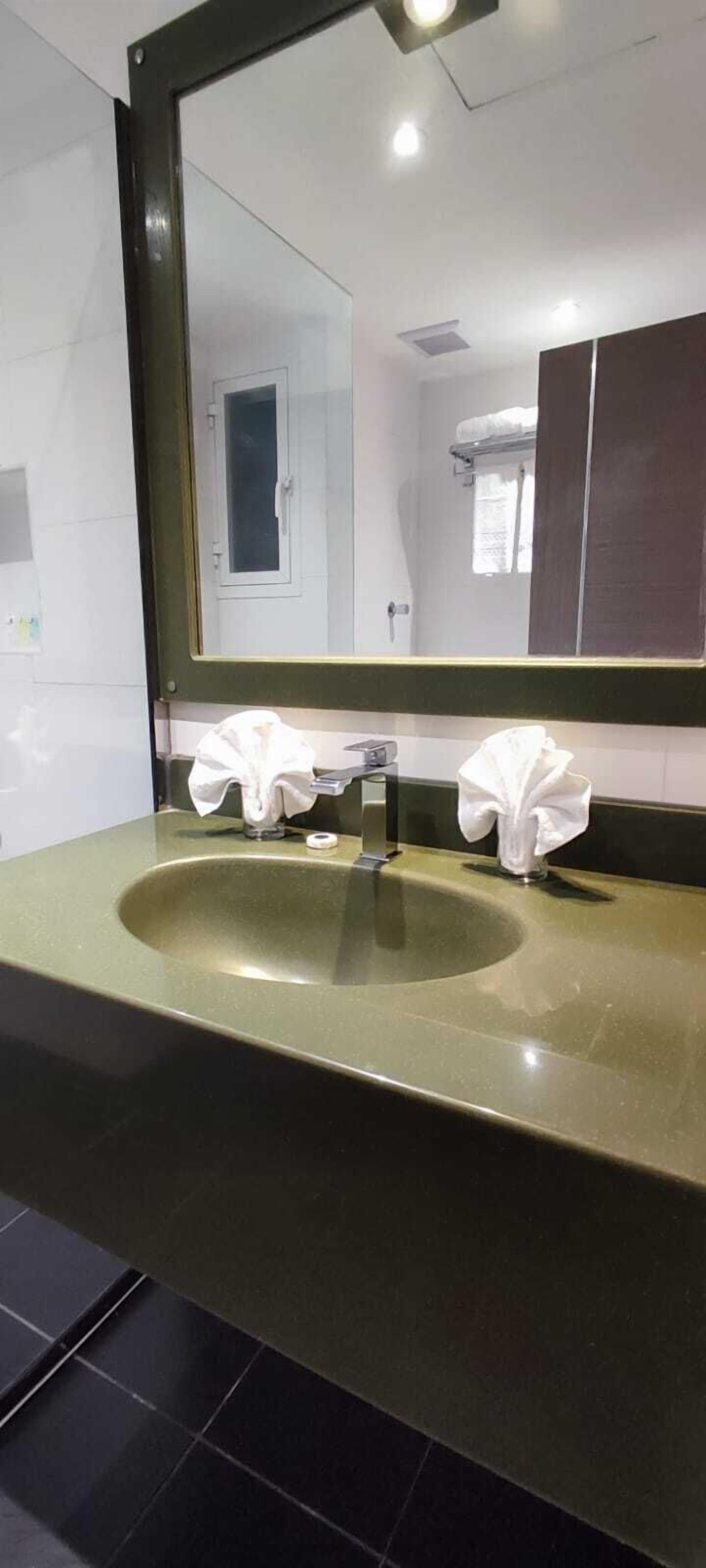 A bathroom with a green sink, a mirror, and two white towels hanging on the wall.