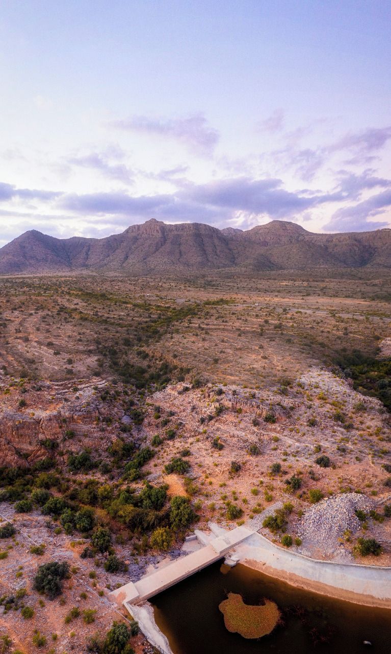 Paisatge de desert amb vegetació escassa i un petit pont sobre una massa d'aigua.
