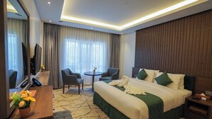 A hotel room with a large bed, a desk with a TV, a small table, and a chair. - GREEN VIEW HOTEL (Sayq)