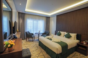 Habitación de hotel con una cama grande, un escritorio con televisor, una mesita pequeña y una silla.