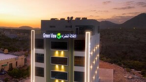 A modern building with a sign reading "Green View" and Arabic text, surrounded by a desert landscape with mountains in the background. - GREEN VIEW HOTEL (Sayq)