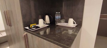 Una encimera de cocina con una cafetera, dos tazas, una botella de agua y un vaso.