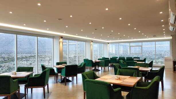 A spacious dining area with green upholstered chairs and tables, large windows offering a view of a cityscape. - GREEN VIEW HOTEL (Sayq)