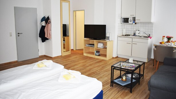 Habitación de hotel con cama, televisión, kitchenette y zona de estar.