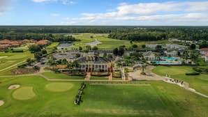 A golf course with a clubhouse, a swimming pool, and residential buildings in the background. - Providence Golf & Country Club Executive Pool Home - Located Near Disney (Davenport)