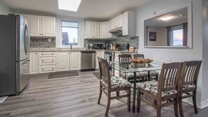 A modern kitchen with white cabinets, a glass dining table, and patterned chairs.
