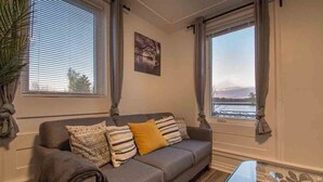 A living room with a grey sofa, a glass coffee table, and a view of a body of water through large windows.
