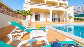 A pool area with lounge chairs and a table, a building with a tiled roof, and a clear blue sky. - Villa w/ Heatable Pool and BBQ in Galé (Albufeira)