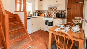 A kitchen with wooden beams, a stove, microwave, and a dining table with chairs. - Walkmill Barn (Bishops Castle)