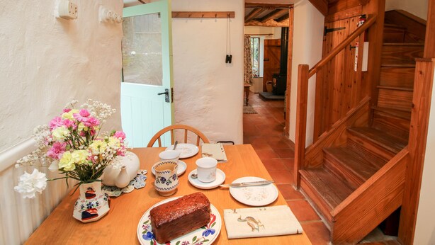 A dining area with a wooden table set for two, a vase of flowers, and a loaf of bread on a plate. - Walkmill Barn (Bishops Castle)