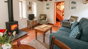 A cozy living room with a fireplace, wooden beams, a sofa, and a television. - Walkmill Barn (Bishops Castle)