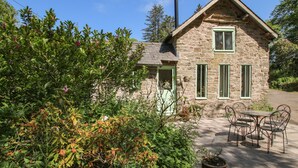 A stone cottage with a chimney, a door, and a window. There is a table and chairs outside. - Walkmill Barn (Bishops Castle)