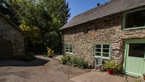 A stone building with a paved courtyard, a green door, and a window with a green frame. - Walkmill Barn (Bishops Castle)