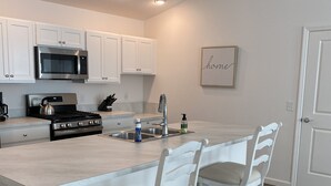 A modern kitchen with white cabinetry, a stainless steel stove, and a large island with bar stools. - 2BR/2BA Patio Villa in the Village of DeLuna (The Villages)
