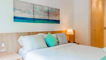 Una habitación de hotel con una cama, una mesita de noche, una lámpara y un cuadro de una playa.