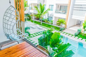 A modern hotel balcony with a wooden table, a hanging chair, and a pool view. - Beach getaway for amazing vacation in Punta Cana (Punta Cana)