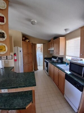 A kitchen with wooden cabinets, a stove, a microwave, and a dishwasher. - Death Valley Passageway Lakeside Cabin A at Lake Olancha (Olancha)