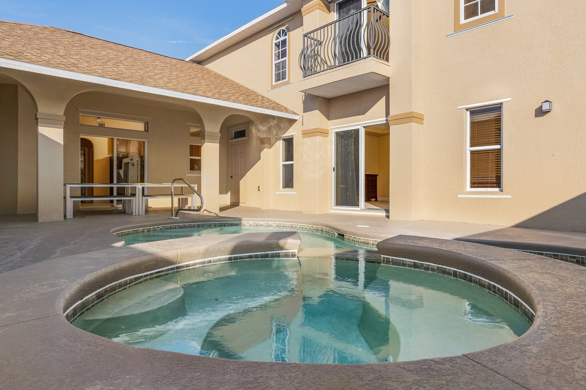 A swimming pool with a curved design, surrounded by a covered patio area with a railing.