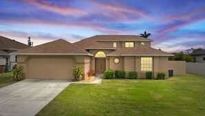 A two-story house with a garage, a front door, and a small front yard with plants.