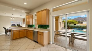 A modern kitchen with wooden cabinets and a large island, leading to a glass door opening to a pool area.