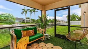 A balcony with a green sofa, wicker chair, and tropical plants.