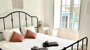 Un lit bien fait, avec une couette blanche et deux serviettes enroulées, un cadre en métal noir et un élément décoratif mural.