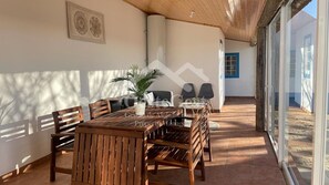 Un patio iluminado por el sol con una mesa y sillas de madera, una planta en maceta y vistas al exterior.