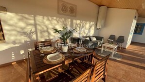 Un coin repas avec une table en bois dressée pour quatre personnes, une plante en pot et un canapé en arrière-plan.