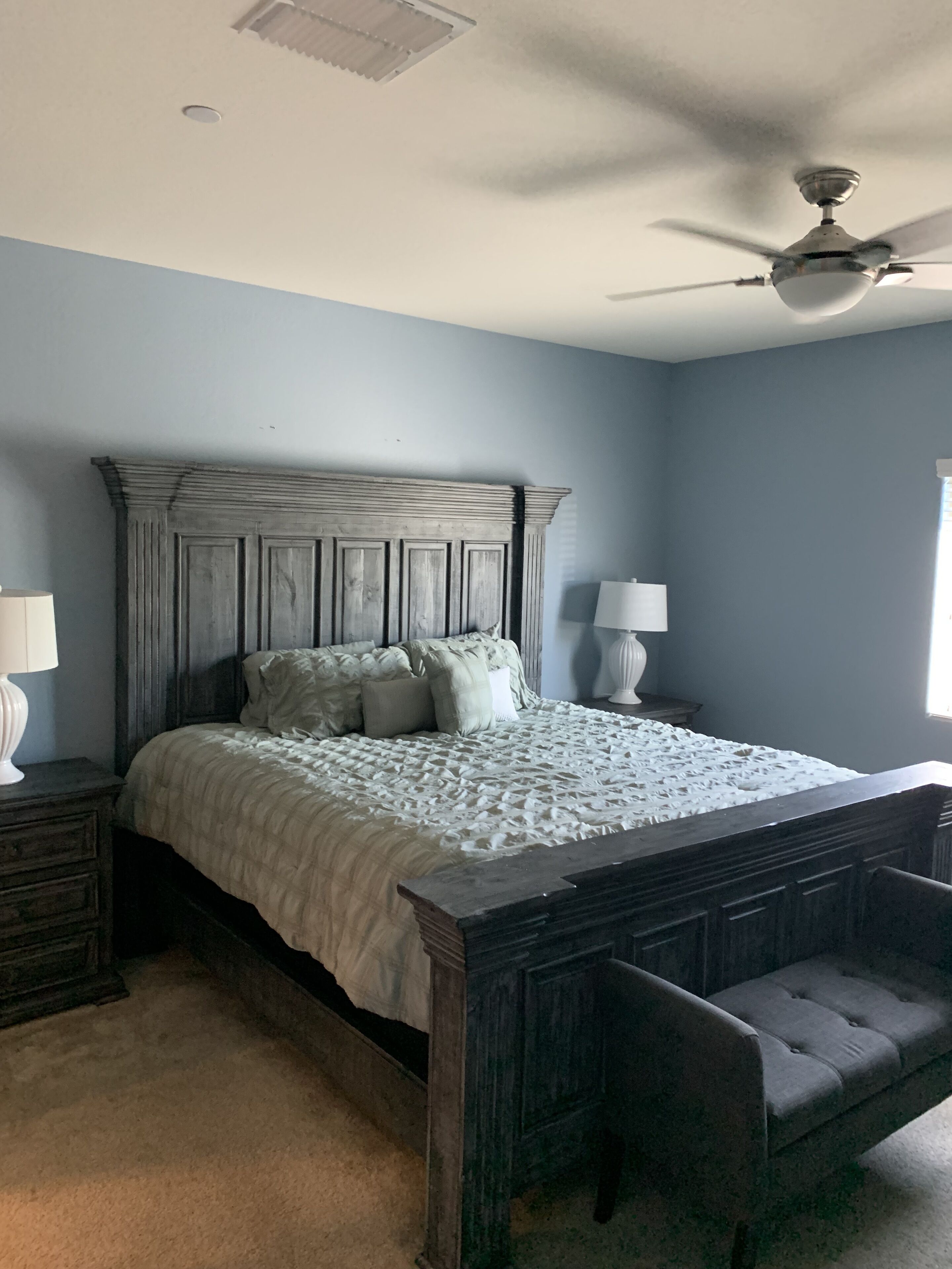 A bedroom with a wooden bed, two bedside tables with lamps, a ceiling fan, and a window.