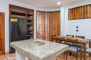 A kitchen with a granite countertop, a stainless steel refrigerator, wooden cabinets, and a dining area with a table and chairs.
