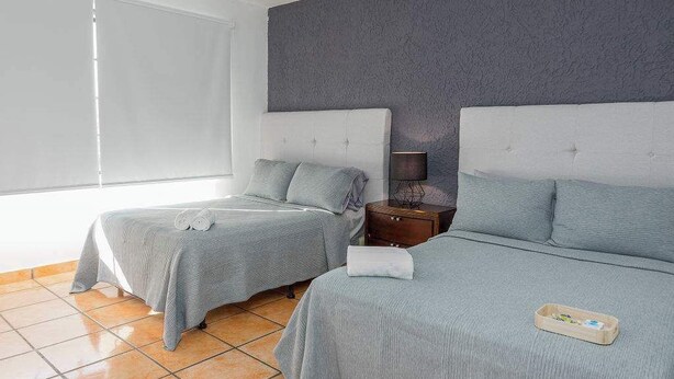 Habitación de hotel con dos camas, una mesita de noche, una lámpara y una ventana con persianas.
