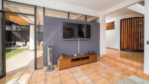 Una sala moderna con un televisor de pantalla plana montado en la pared, un mueble de madera para entretenimiento y un amplio ventanal corredizo que da a un área exterior.