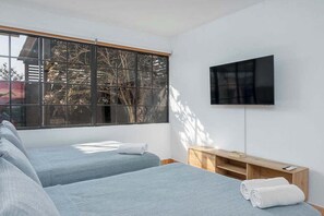 A room with two beds, a TV, and a window with a view of trees. - New, in the heart of the city, 5 min to US Embassy (Antiguo Cuscatlán)