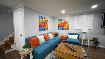 Un salon moderne avec un canapé bleu, des tableaux abstraits aux couleurs vives, une table basse en bois et un escalier.