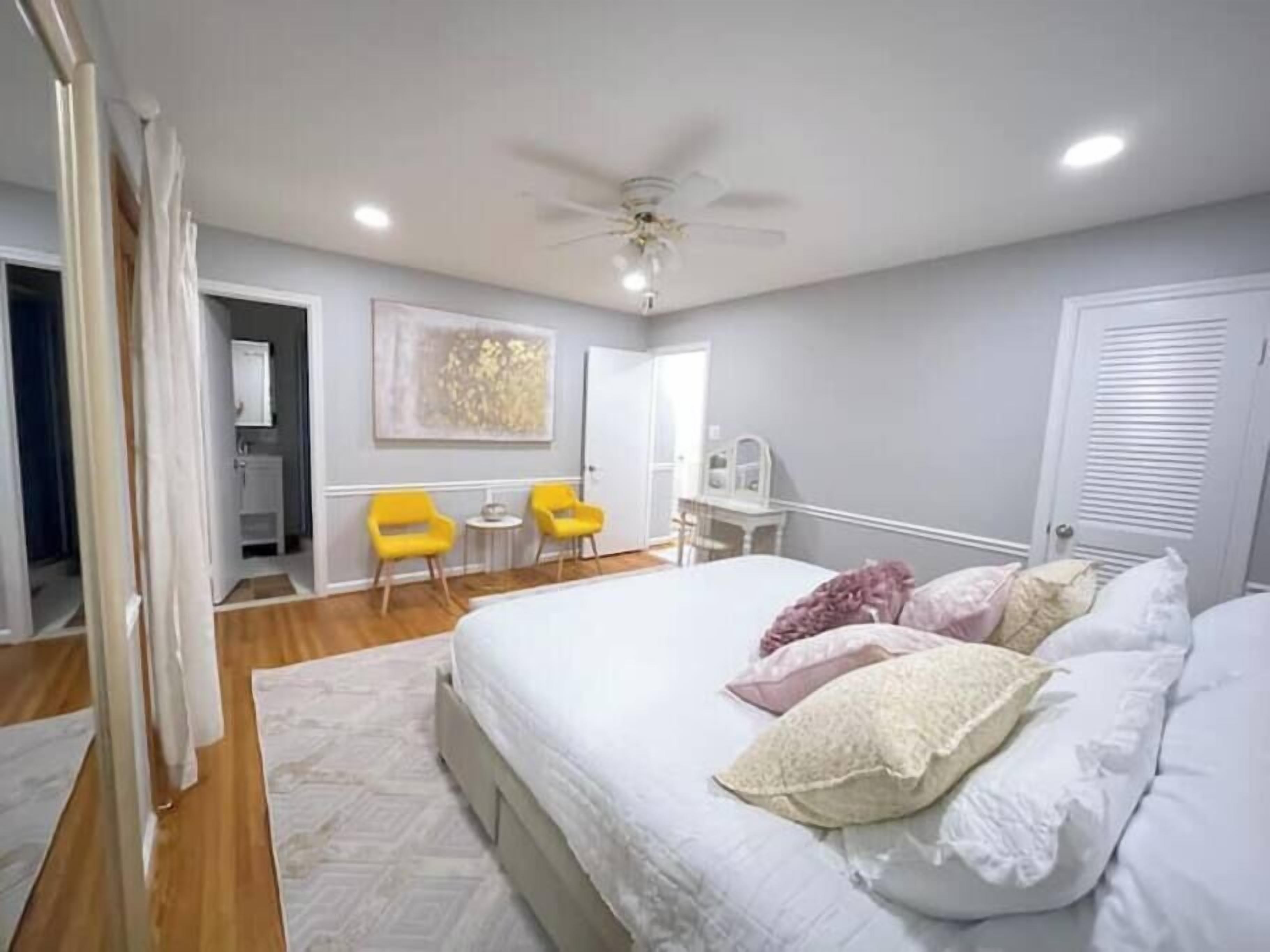 Une chambre à coucher avec un lit, un ventilateur de plafond, un bureau, une chaise et une porte.