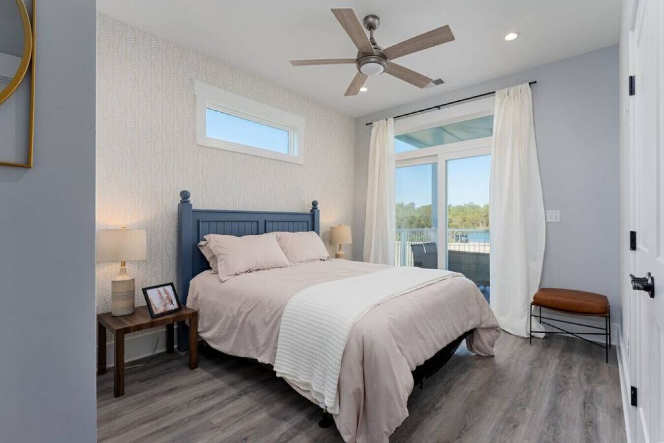 A bedroom with a large bed, a ceiling fan, a window, and a view of the outdoors.