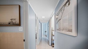 Un couloir aux murs bleu clair, doté d’un sol carrelé et orné d’œuvres d’art encadrées.
