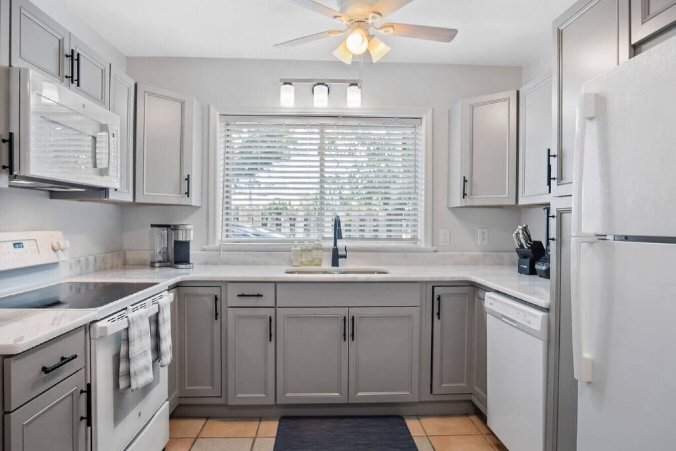 A modern kitchen with grey cabinets, a built-in oven, a sink, and a ceiling fan.