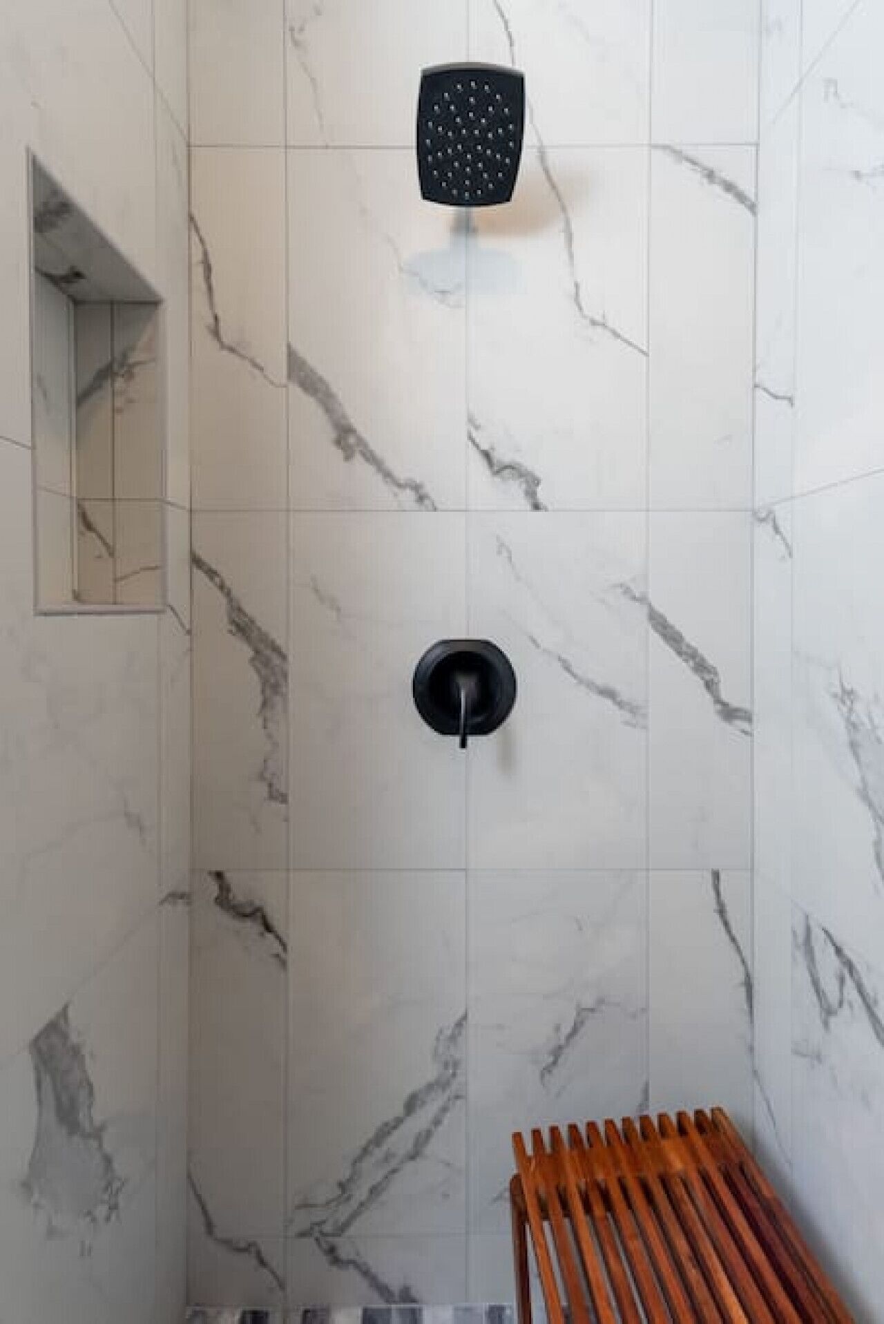 A shower area with a marble wall, a handheld showerhead, and a wooden bench.