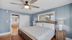 Un dormitorio con una cama, una mesita de noche, una lámpara, un ventilador de techo y una ventana.
