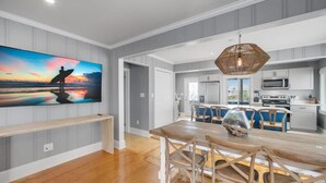 A modern kitchen with white cabinets, a central island, and a dining area with a wooden table and chairs. - A Swell Life | Walking Distance to Ocean w/ King B (Wrightsville Beach)