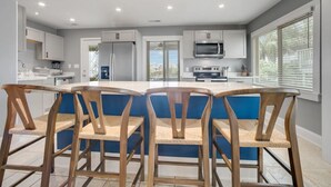 A modern kitchen with a central island, white cabinets, and a large window. - A Swell Life | Walking Distance to Ocean w/ King B (Wrightsville Beach)