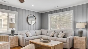 A living room with a sectional sofa, two side tables, a coffee table, and a round mirror on the wall. - A Swell Life | Walking Distance to Ocean w/ King B (Wrightsville Beach)