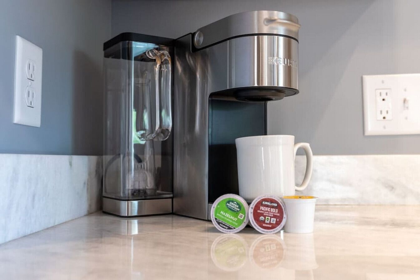 A coffee maker, a mug, and two containers of coffee creamer on a kitchen counter.