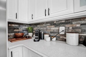 Kitchen features white cabinetry with black handles, a brick-patterned backsplash, and a wooden cutting board.