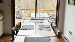 A dining area with a wooden table and chairs, a view of a deck and trees outside. - Lake Harmony, 4BR, Lake Access, Kayak, Woods, Air Hockey, New Water Treat System (Lake Harmony)